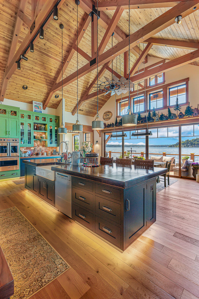 Mid-sized mountain style u-shaped medium tone wood floor, brown floor and vaulted ceiling open concept kitchen photo in Seattle with a farmhouse sink, recessed-panel cabinets, green cabinets, soapstone countertops, white backsplash, porcelain backsplash, stainless steel appliances, an island and black countertops