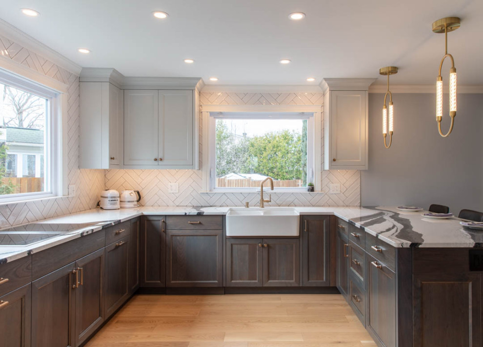 Open concept kitchen - transitional u-shaped light wood floor open concept kitchen idea in Ottawa with a farmhouse sink, recessed-panel cabinets, dark wood cabinets, quartz countertops, white backsplash, porcelain backsplash, paneled appliances, a peninsula and black countertops