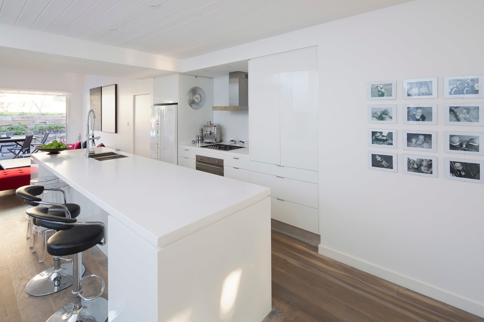 Design ideas for a mid-sized contemporary galley open plan kitchen in Sydney with an undermount sink, flat-panel cabinets, white cabinets, quartz benchtops, white splashback, glass sheet splashback, stainless steel appliances, light hardwood floors, with island, brown floor and yellow benchtop.