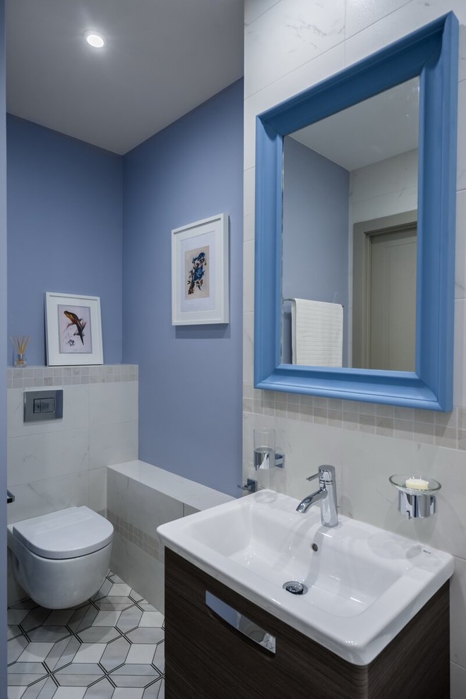 Transitional powder room in Saint Petersburg with flat-panel cabinets, dark wood cabinets, a wall-mount toilet, white tile, blue walls, an integrated sink and grey floor.