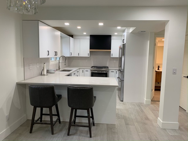 Inspiration for a contemporary l-shaped kitchen remodel in New York with a drop-in sink, flat-panel cabinets, white cabinets, granite countertops and black appliances