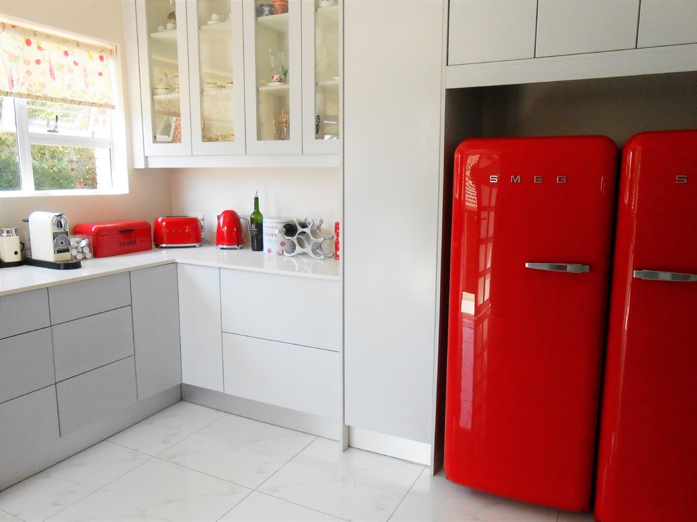 Mid-sized modern l-shaped eat-in kitchen in Other with a farmhouse sink, flat-panel cabinets, grey cabinets, granite benchtops, red splashback, stone slab splashback, coloured appliances, porcelain floors and no island.