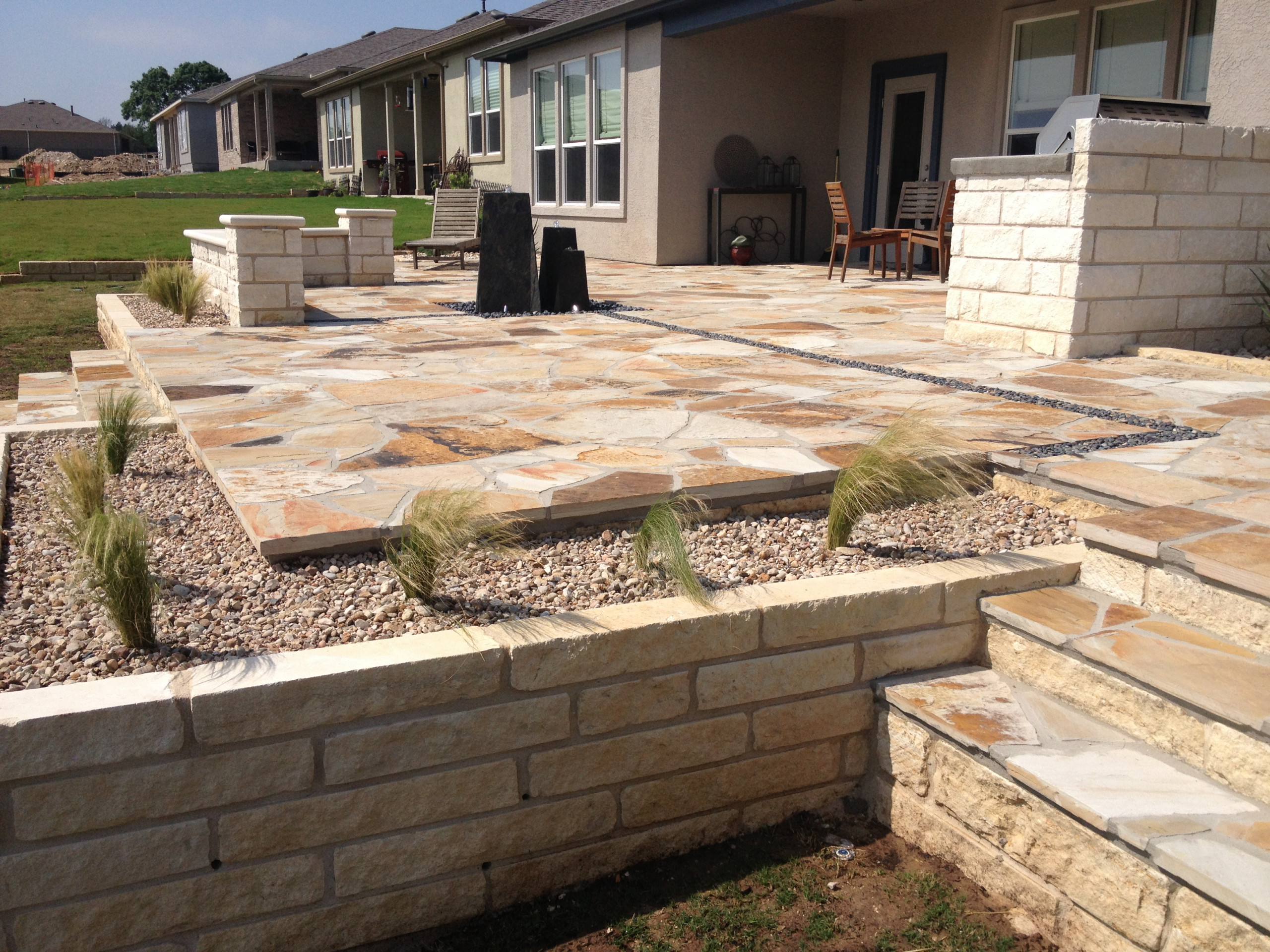 Modern flagstone patio with water feature, basalt inlays, raised limestone beds