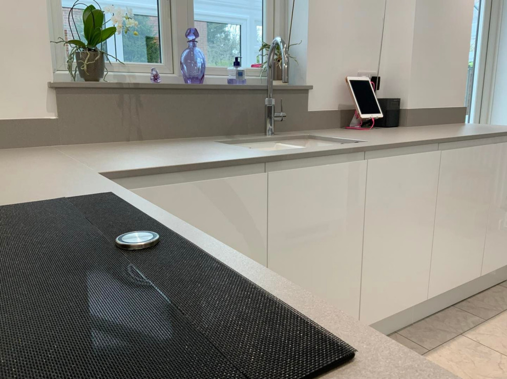 This is an example of a medium sized contemporary grey and white u-shaped kitchen with flat-panel cabinets, white cabinets, quartz worktops, pink splashback, glass sheet splashback, integrated appliances, no island and grey worktops.