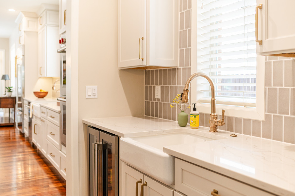 Example of a large transitional l-shaped dark wood floor and brown floor open concept kitchen design in Denver with a farmhouse sink, shaker cabinets, beige cabinets, quartz countertops, beige backsplash, ceramic backsplash, stainless steel appliances, an island and white countertops