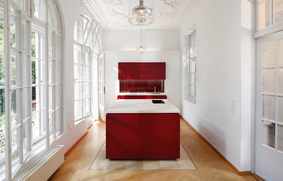 Photo of a mid-sized traditional separate kitchen in Munich with an undermount sink, flat-panel cabinets, red cabinets, red splashback, glass sheet splashback, panelled appliances, light hardwood floors and with island.
