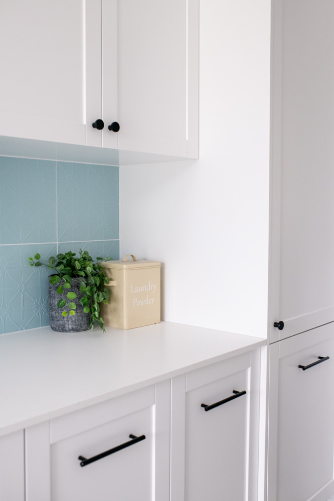 Modern inredning av en stor vita parallell vitt tvättstuga enbart för tvätt, med en nedsänkt diskho, skåp i shakerstil, vita skåp, bänkskiva i kvarts, blått stänkskydd, stänkskydd i keramik, blå väggar, klinkergolv i keramik, en tvättmaskin och torktumlare bredvid varandra och grått golv