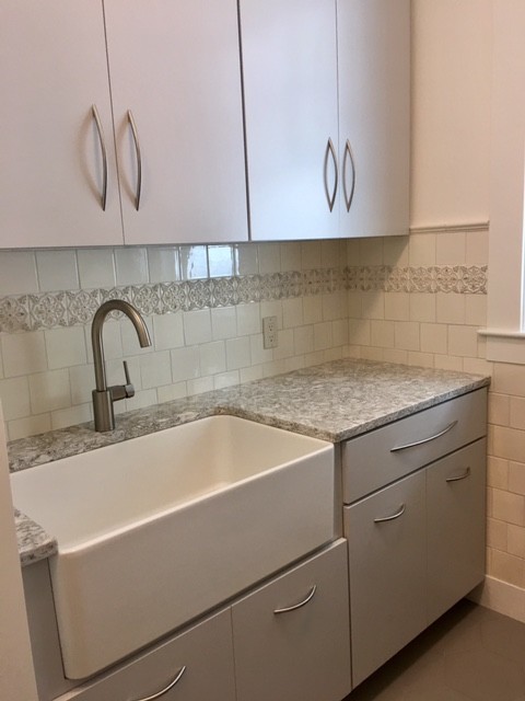 Mid-sized traditional single-wall dedicated laundry room in Portland Maine with flat-panel cabinets, grey cabinets, quartz benchtops, white walls, porcelain floors, a side-by-side washer and dryer, brown floor and a farmhouse sink.