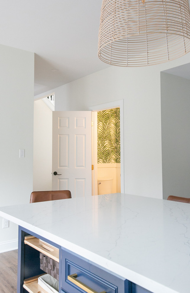 Inspiration for a large transitional l-shaped brown floor kitchen pantry remodel in Baltimore with a drop-in sink, shaker cabinets, white cabinets, quartz countertops, white backsplash, ceramic backsplash, stainless steel appliances, an island and white countertops