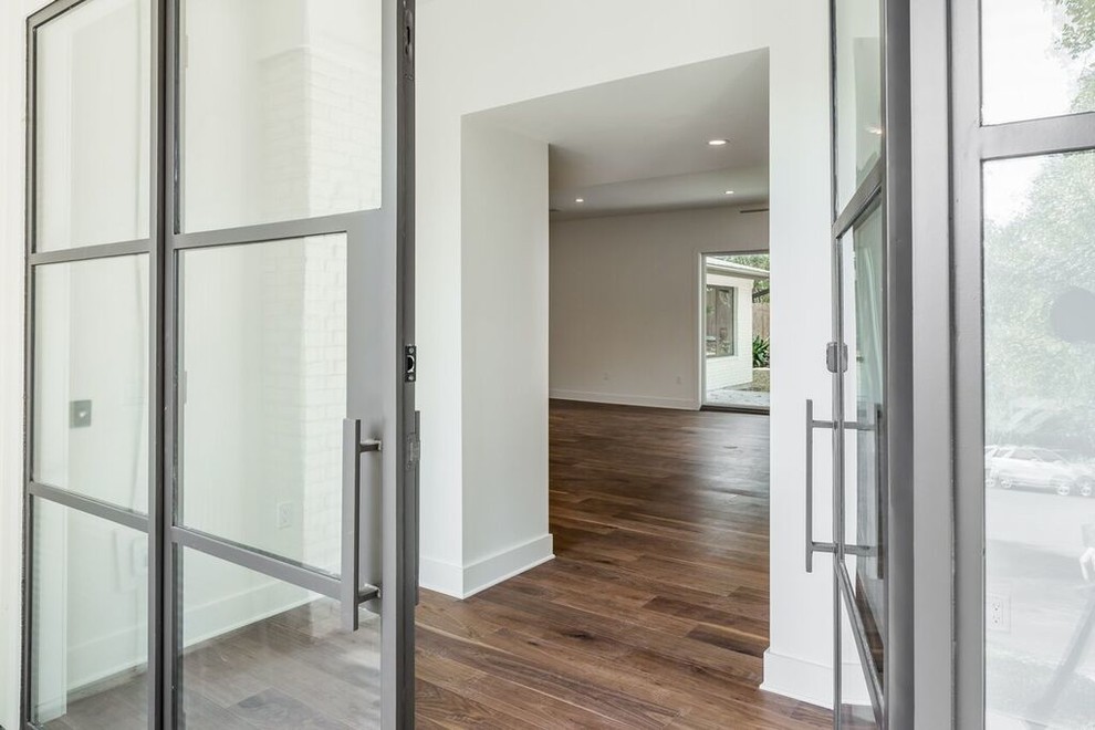 Example of a transitional medium tone wood floor front door design in Austin with white walls and a glass front door
