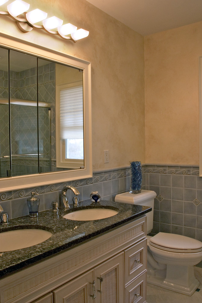 Small beach style bathroom in Bridgeport with an undermount sink, furniture-like cabinets, distressed cabinets, granite benchtops, an alcove tub, a shower/bathtub combo, a two-piece toilet, blue tile, porcelain tile, beige walls and porcelain floors.