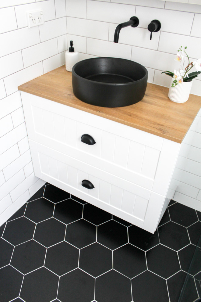 This is an example of a small modern kids bathroom in Perth with shaker cabinets, white cabinets, an open shower, a one-piece toilet, white tile, ceramic tile, white walls, porcelain floors, a vessel sink, wood benchtops, black floor, an open shower, beige benchtops, a single vanity, a floating vanity and brick walls.