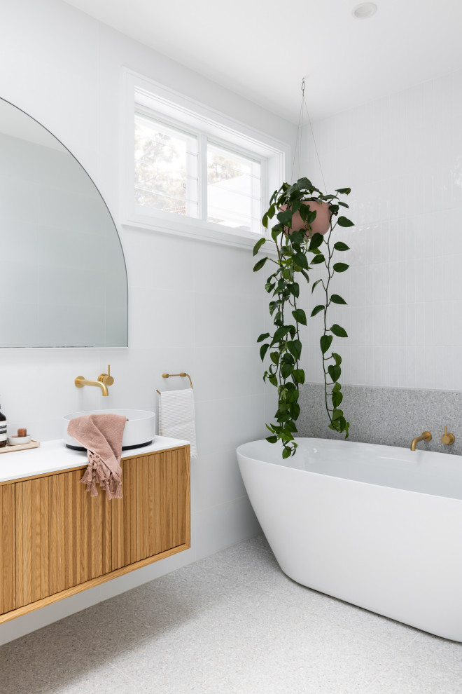 Modernes Badezimmer En Suite mit hellbraunen Holzschränken, freistehender Badewanne, Toilette mit Aufsatzspülkasten, weißen Fliesen, Keramikfliesen, weißer Wandfarbe, Terrazzo-Boden, grauem Boden, weißer Waschtischplatte, Doppelwaschbecken und schwebendem Waschtisch in Sydney