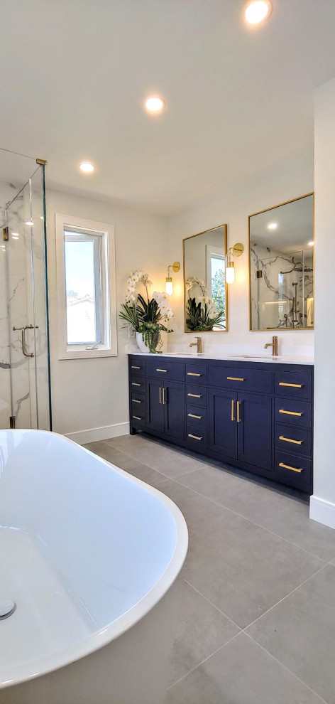 Bild på ett funkis vit vitt badrum, med skåp i shakerstil, blå skåp, ett fristående badkar, en hörndusch, vit kakel, porslinskakel, klinkergolv i porslin, bänkskiva i kvarts, grått golv och dusch med gångjärnsdörr