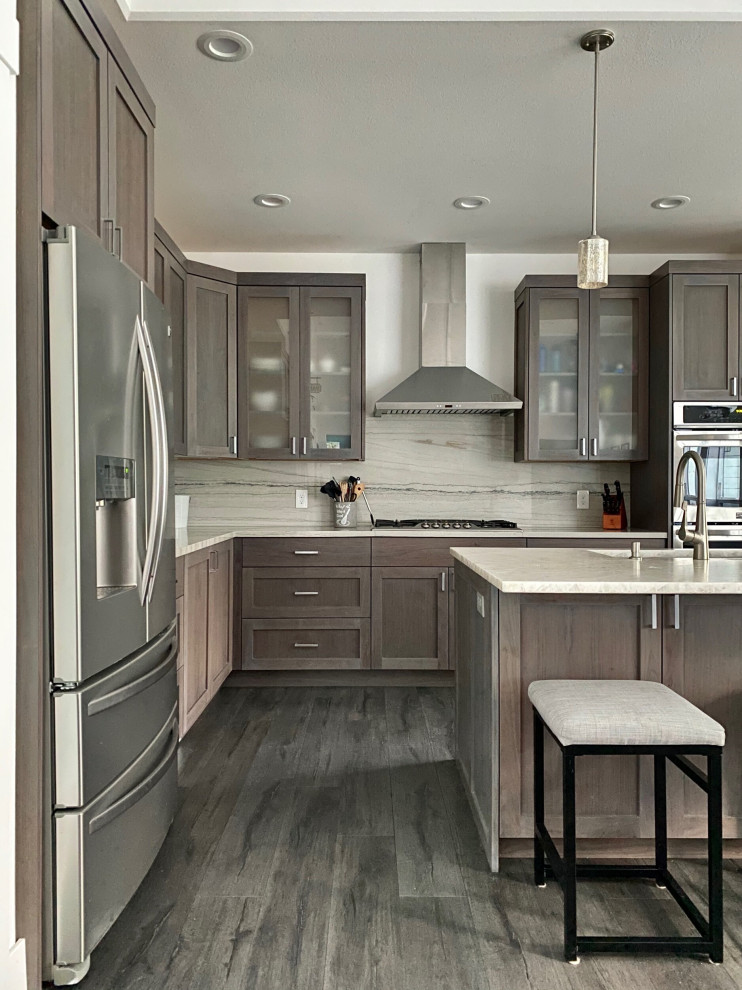 Example of a minimalist l-shaped vinyl floor and brown floor open concept kitchen design in Seattle with a farmhouse sink, raised-panel cabinets, brown cabinets, marble countertops, white backsplash, granite backsplash, stainless steel appliances, an island and white countertops