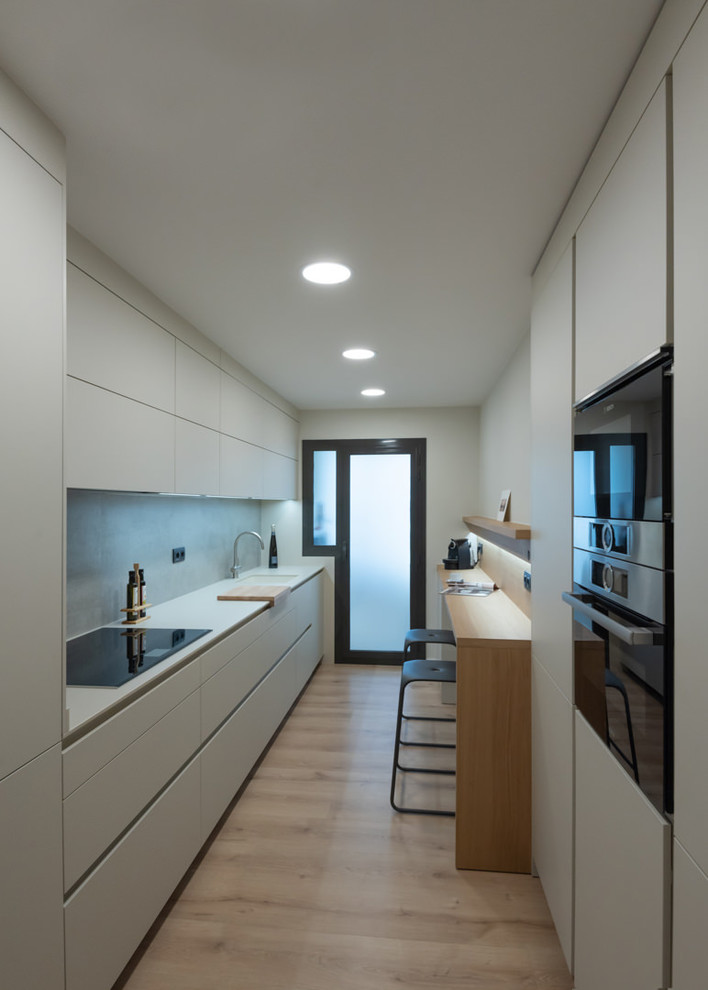 Design ideas for a mid-sized contemporary galley separate kitchen in Barcelona with an integrated sink, flat-panel cabinets, beige cabinets, grey splashback, panelled appliances, light hardwood floors, no island, brown floor and beige benchtop.