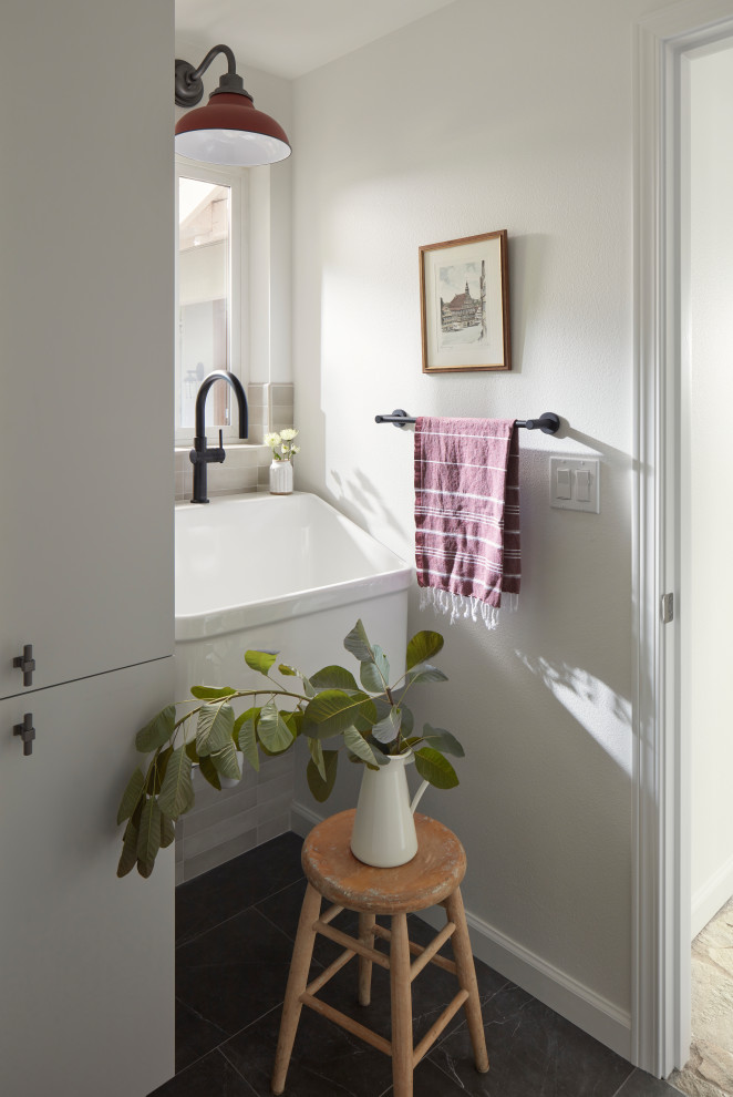 This is an example of a small traditional separated utility room in Seattle with an utility sink, flat-panel cabinets, grey cabinets, beige splashback, ceramic splashback, white walls, porcelain flooring, a stacked washer and dryer and black floors.