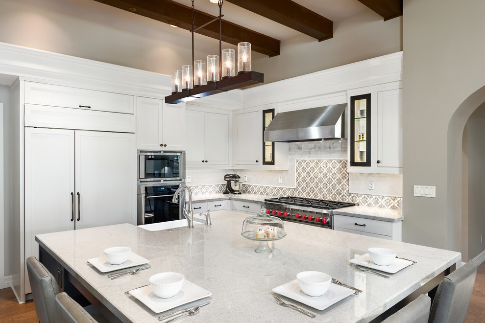 Kitchen - large transitional l-shaped light wood floor and brown floor kitchen idea in Phoenix with a farmhouse sink, shaker cabinets, white cabinets, granite countertops, white backsplash, porcelain backsplash, stainless steel appliances and an island