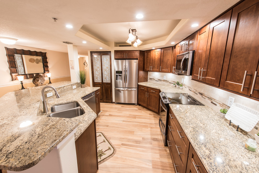 Inspiration for a mid-sized transitional porcelain tile eat-in kitchen remodel with an undermount sink, shaker cabinets, dark wood cabinets, granite countertops, beige backsplash, stone tile backsplash, stainless steel appliances and an island