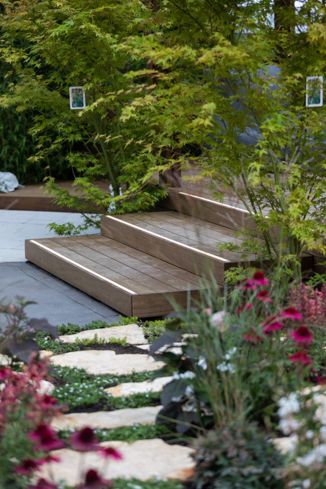 Garten im Sommer mit Pergola, Natursteinplatten und Holzzaun