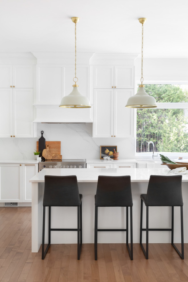 Inspiration for a large transitional l-shaped open plan kitchen in Montreal with an undermount sink, shaker cabinets, white cabinets, quartz benchtops, white splashback, engineered quartz splashback, stainless steel appliances, medium hardwood floors, with island, brown floor, white benchtop and coffered.