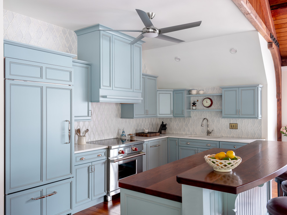 Photo of a traditional u-shaped kitchen in Boston with an undermount sink, recessed-panel cabinets, blue cabinets, grey splashback, stainless steel appliances, medium hardwood floors, with island, brown floor and white benchtop.