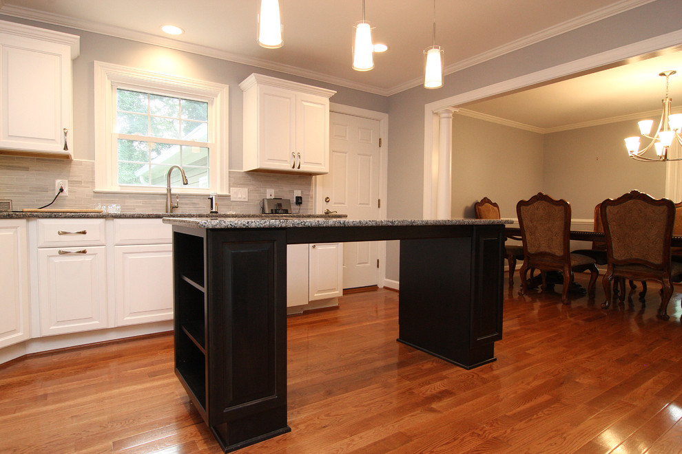 Mid-sized transitional u-shaped medium tone wood floor eat-in kitchen photo with an undermount sink, raised-panel cabinets, white cabinets, granite countertops, gray backsplash, porcelain backsplash, white appliances and an island
