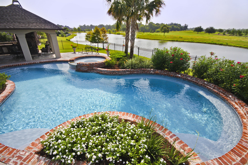 Photo of a large traditional backyard custom-shaped pool in New Orleans with a hot tub and brick pavers.