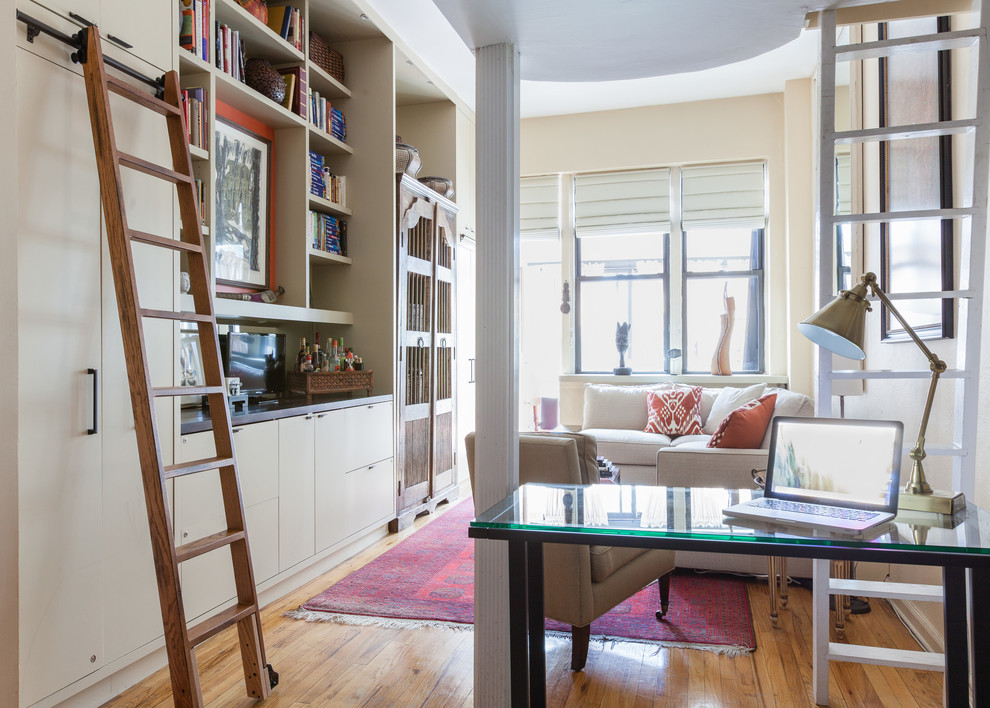 This is an example of a small eclectic open concept living room in New York with a library, white walls, light hardwood floors and a built-in media wall.