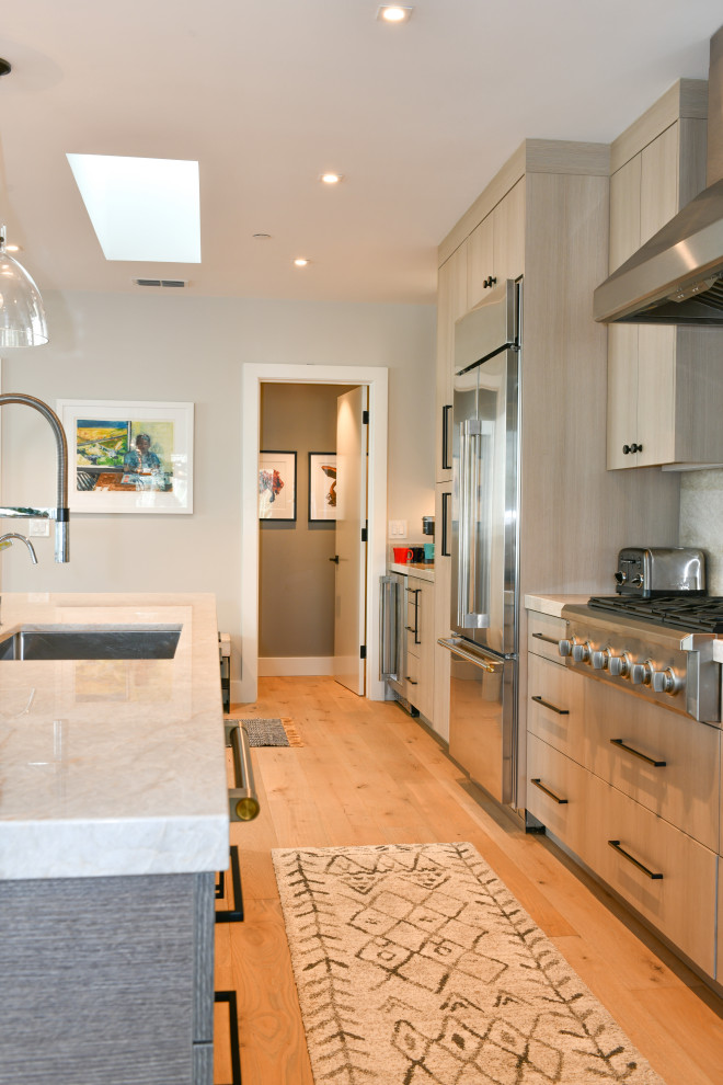 Expansive transitional galley open plan kitchen in San Francisco with a drop-in sink, flat-panel cabinets, grey cabinets, quartzite benchtops, white splashback, marble splashback, stainless steel appliances, light hardwood floors, with island, beige floor and white benchtop.