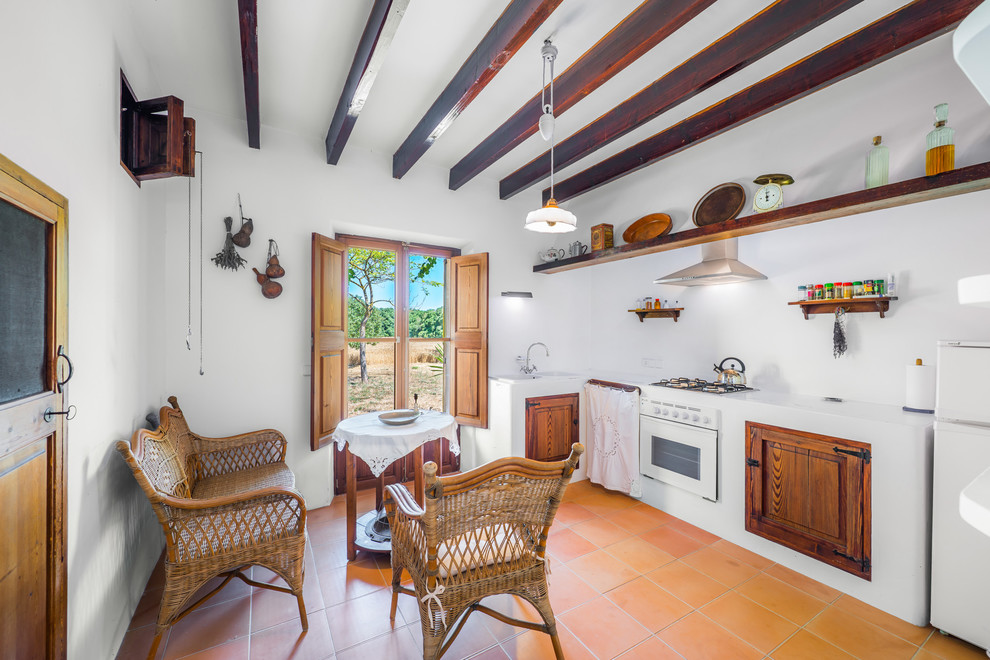 Inspiration for a mid-sized country l-shaped separate kitchen in Palma de Mallorca with raised-panel cabinets, medium wood cabinets, solid surface benchtops, white splashback, stainless steel appliances, terra-cotta floors and no island.
