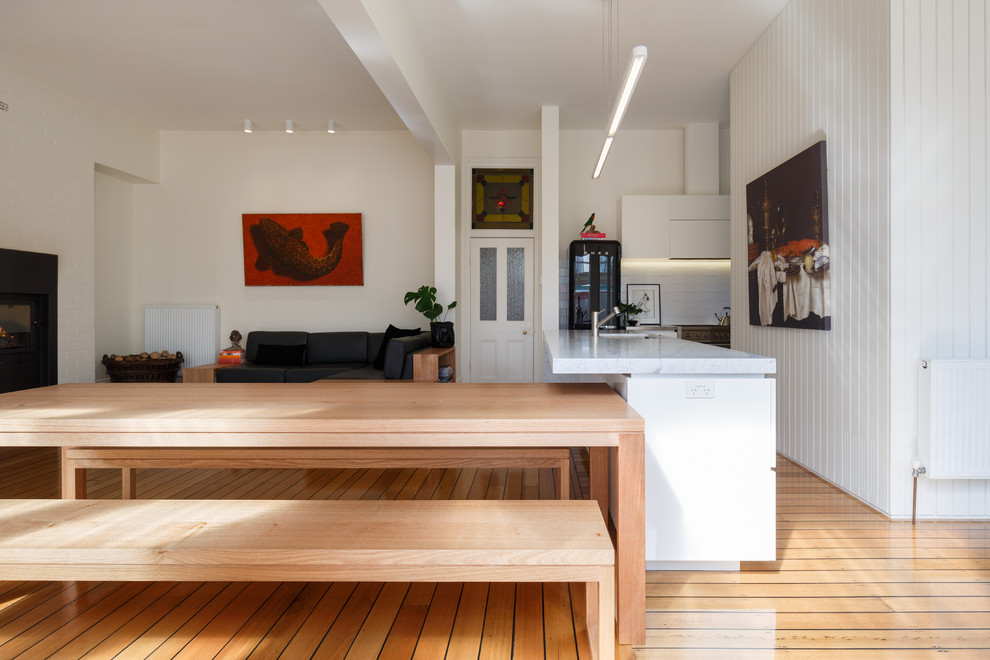 Design ideas for a mid-sized traditional u-shaped eat-in kitchen in Hobart with an integrated sink, flat-panel cabinets, white cabinets, marble benchtops, white splashback, ceramic splashback, black appliances, light hardwood floors and with island.