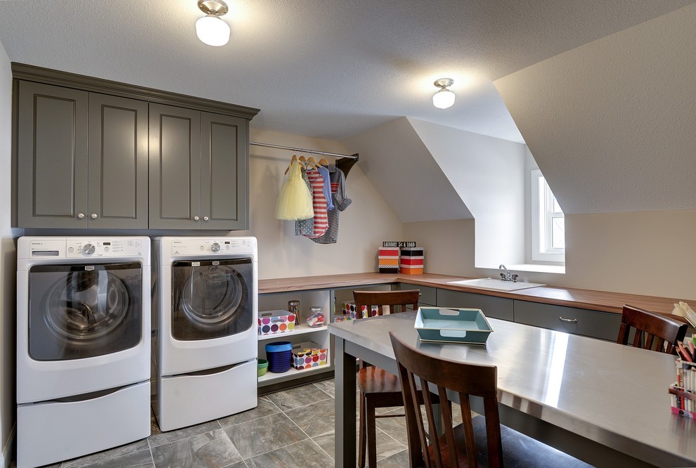 Large traditional l-shaped utility room in Minneapolis with grey cabinets, wood benchtops, beige walls, a side-by-side washer and dryer, a drop-in sink, recessed-panel cabinets, grey floor and beige benchtop.