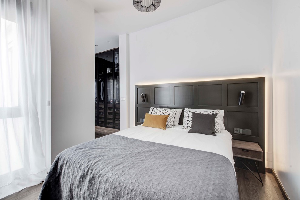 Photo of a mid-sized industrial master bedroom in Madrid with white walls, laminate floors and brown floor.