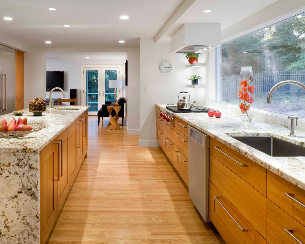 This is an example of a large transitional galley kitchen in Boston with shaker cabinets, stainless steel appliances, an undermount sink, medium wood cabinets, granite benchtops, window splashback, light hardwood floors and with island.