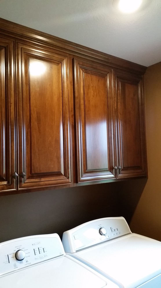 This is an example of a mid-sized traditional laundry room in Other with raised-panel cabinets, medium wood cabinets, granite benchtops, ceramic floors, brown walls and a side-by-side washer and dryer.