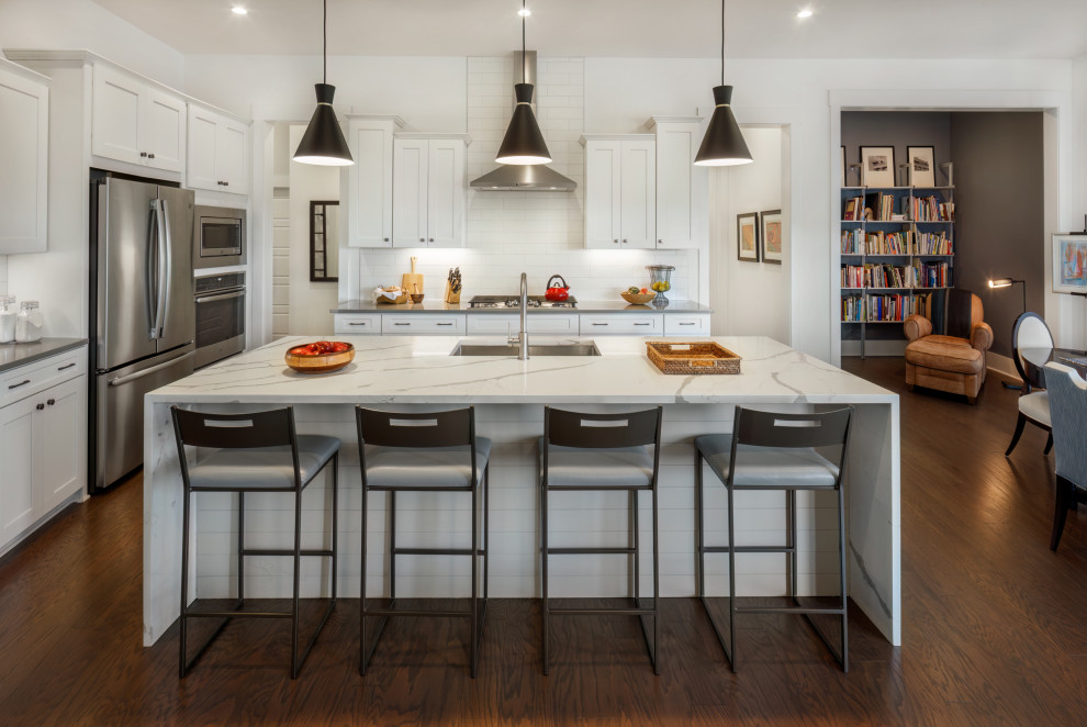 Design ideas for a mid-sized transitional l-shaped open plan kitchen in Charlotte with a single-bowl sink, shaker cabinets, white cabinets, quartz benchtops, white splashback, porcelain splashback, stainless steel appliances, dark hardwood floors, with island, brown floor and multi-coloured benchtop.