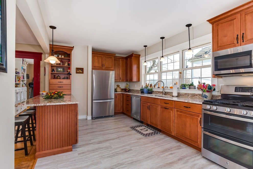 Mid-sized country u-shaped eat-in kitchen in Providence with an undermount sink, raised-panel cabinets, brown cabinets, granite benchtops, beige splashback, stainless steel appliances, vinyl floors, a peninsula and grey floor.