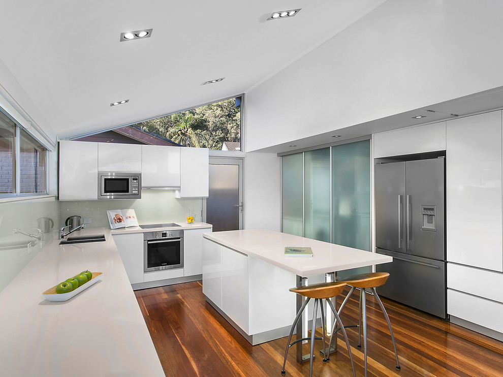 Design ideas for a contemporary u-shaped separate kitchen in Sydney with an undermount sink, flat-panel cabinets, white cabinets, white splashback, glass sheet splashback, stainless steel appliances, medium hardwood floors, with island and brown floor.
