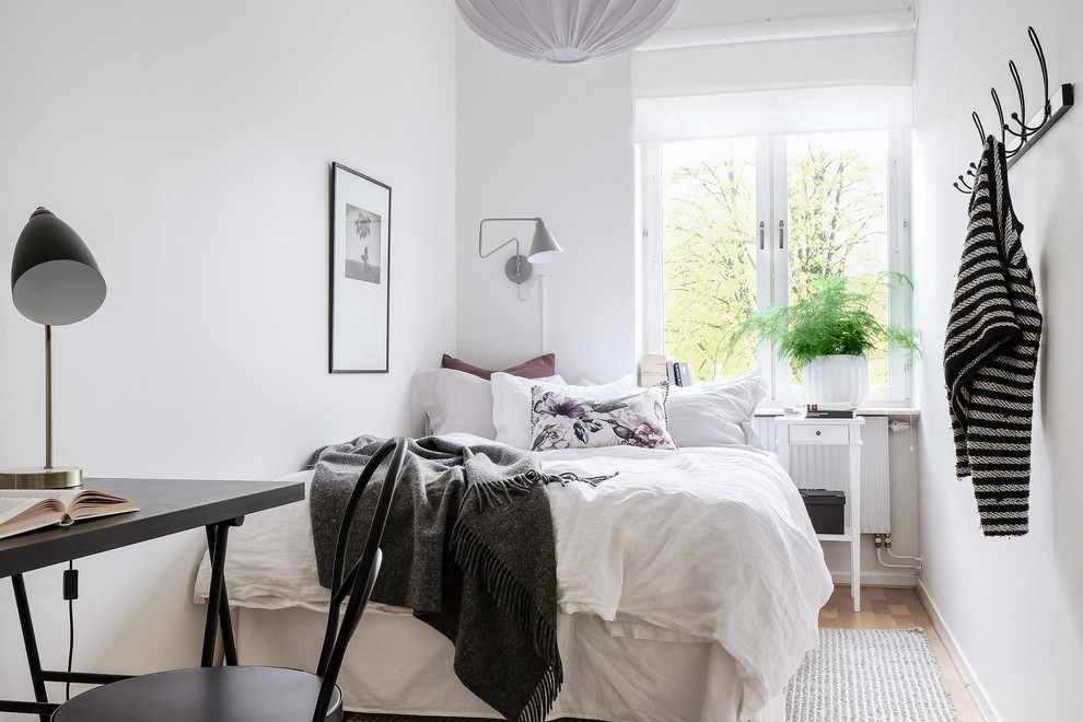 This is an example of a scandinavian bedroom in Gothenburg with white walls, medium hardwood floors, no fireplace and brown floor.
