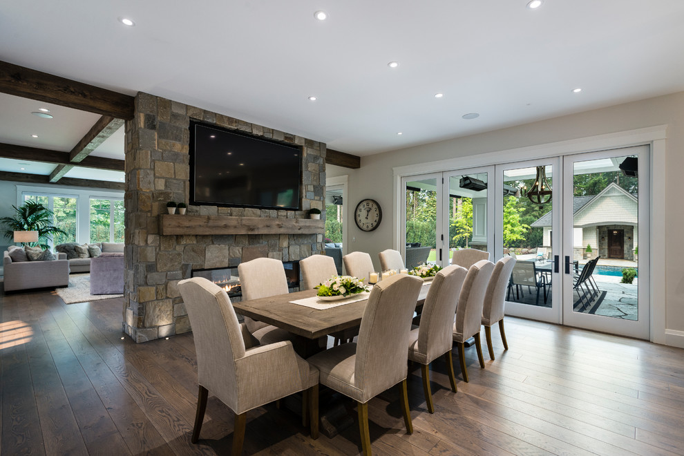 This is an example of an expansive traditional open plan dining in Vancouver with grey walls, medium hardwood floors, a two-sided fireplace, a stone fireplace surround and brown floor.