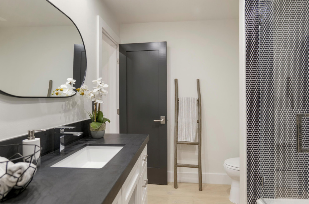 Cette photo montre une salle de bain tendance avec un placard à porte shaker, des portes de placard blanches, un carrelage noir, un plan de toilette noir, meuble simple vasque et meuble-lavabo encastré.