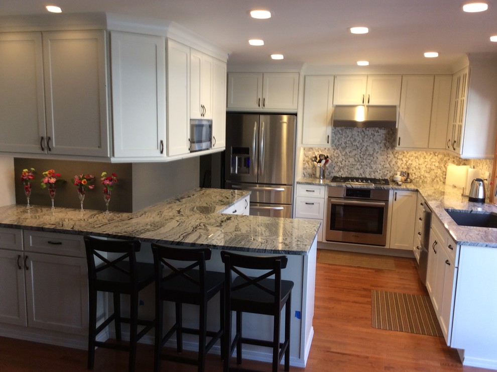 Example of a mid-sized transitional l-shaped medium tone wood floor kitchen pantry design in Denver with an undermount sink, shaker cabinets, white cabinets, granite countertops, gray backsplash, ceramic backsplash and stainless steel appliances