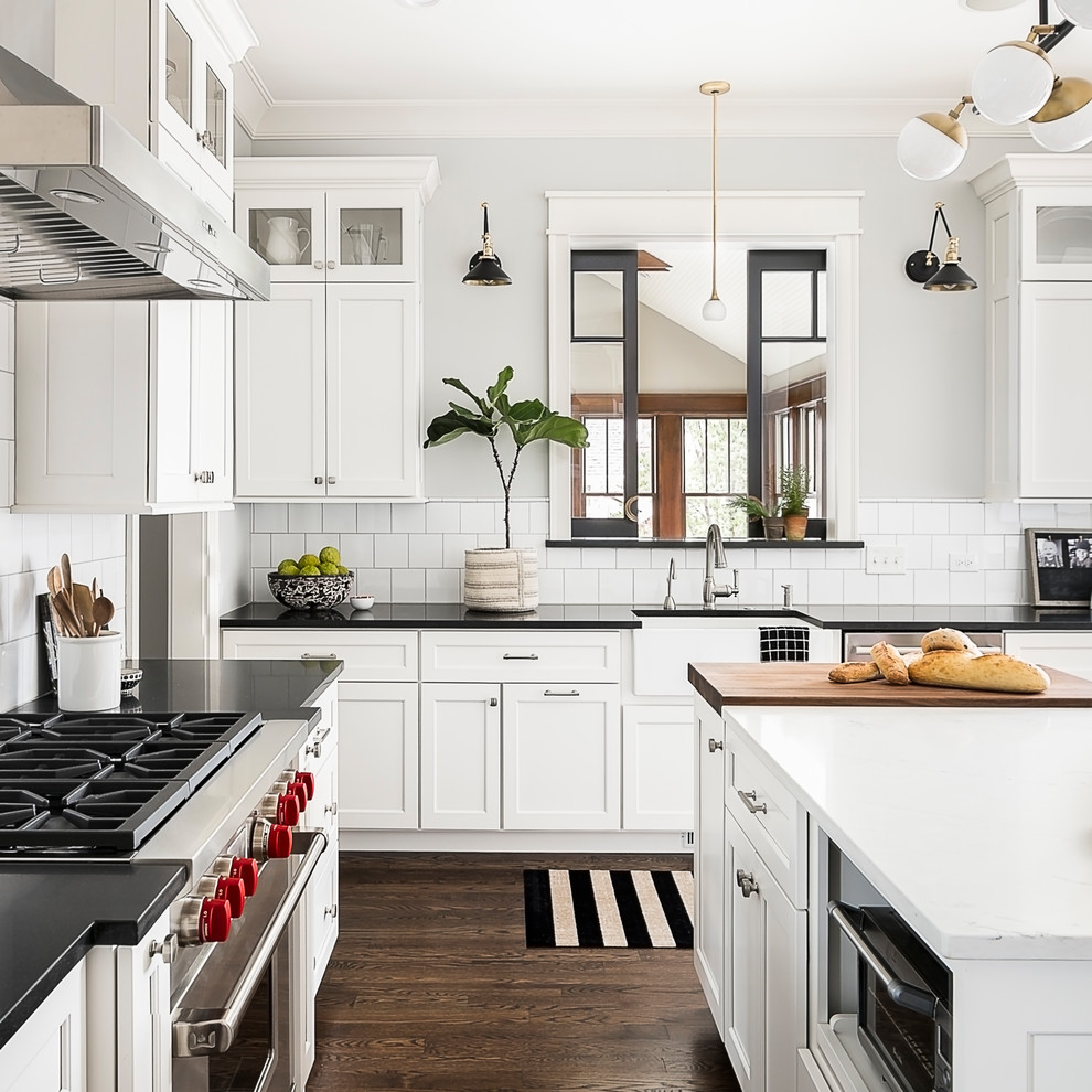 Mid-sized transitional u-shaped eat-in kitchen in Chicago with a farmhouse sink, shaker cabinets, white cabinets, quartz benchtops, white splashback, ceramic splashback, stainless steel appliances, dark hardwood floors, with island and brown floor.