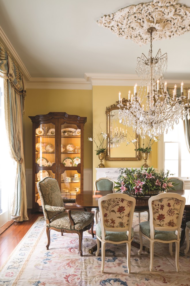 Large traditional dining room in New Orleans with yellow walls, medium hardwood floors, a standard fireplace, a stone fireplace surround and brown floor.