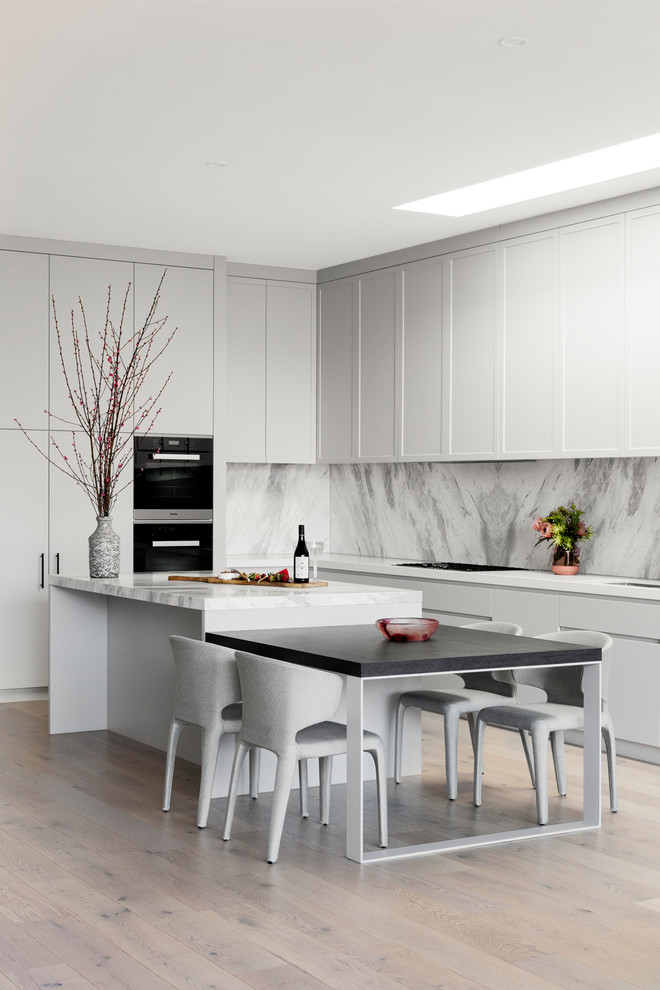 Design ideas for a contemporary l-shaped kitchen in Melbourne with shaker cabinets, white cabinets, grey splashback, stone slab splashback, black appliances, light hardwood floors, with island, beige floor and white benchtop.
