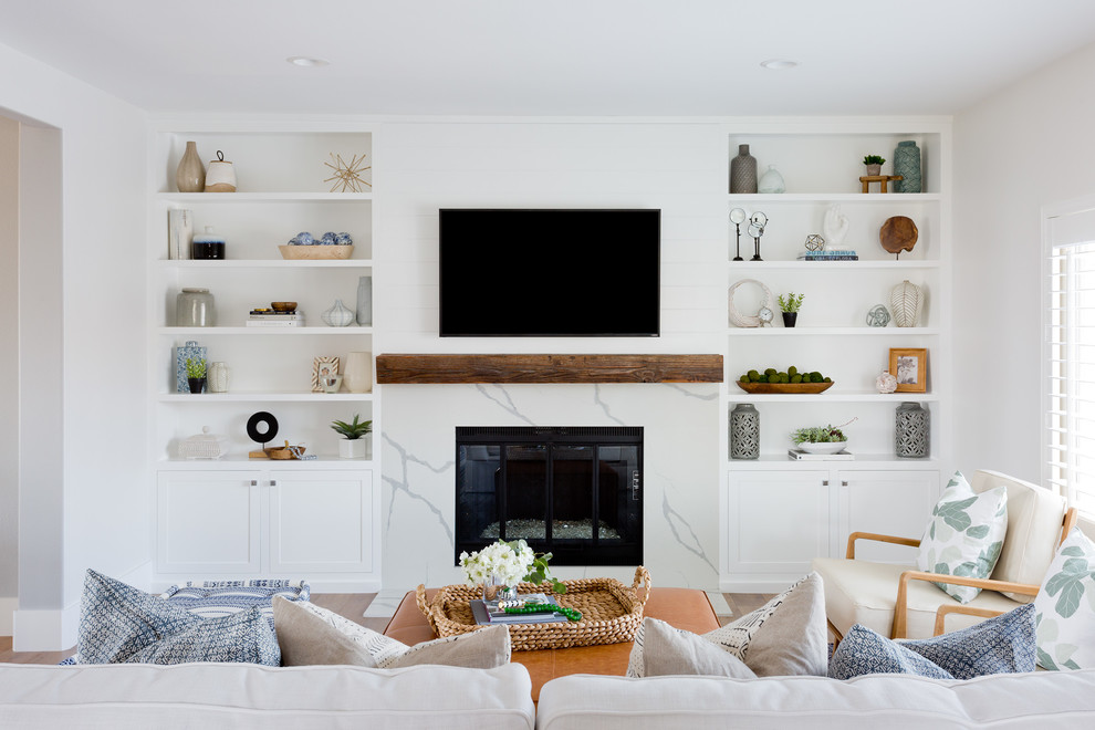 This is an example of a beach style enclosed family room in Orange County with white walls, medium hardwood floors, a standard fireplace, a wall-mounted tv and brown floor.