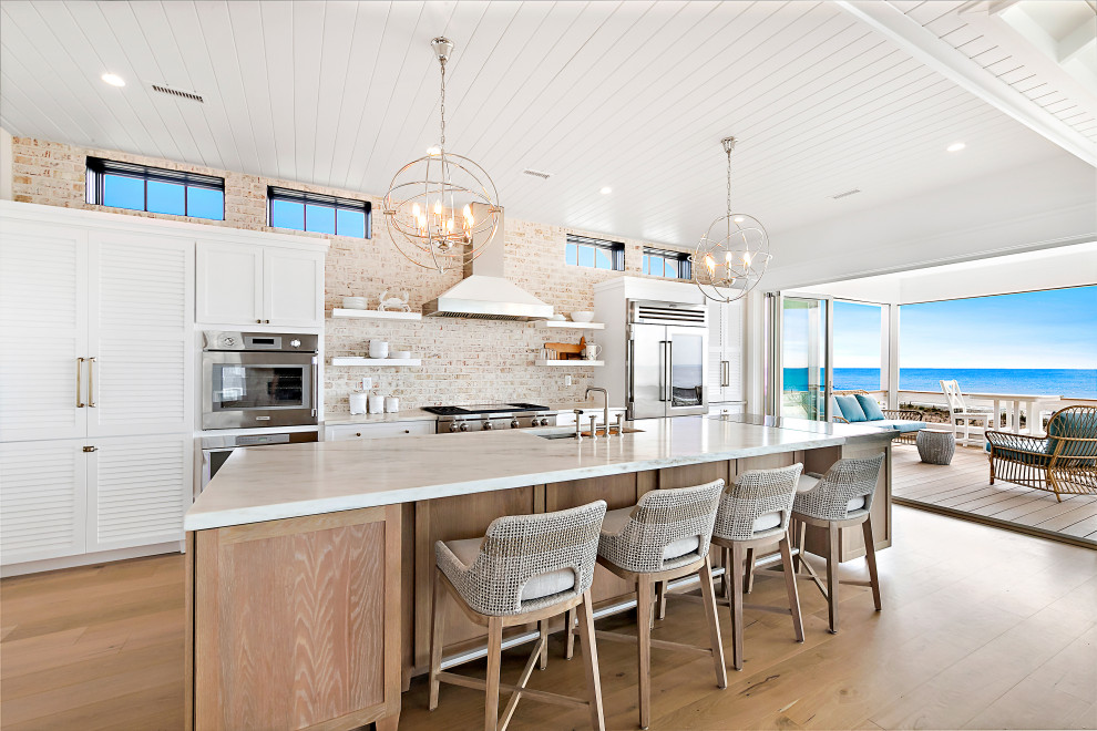 ニューヨークにあるビーチスタイルのおしゃれなアイランドキッチン (レンガのキッチンパネル、シルバーの調理設備、塗装板張りの天井) の写真