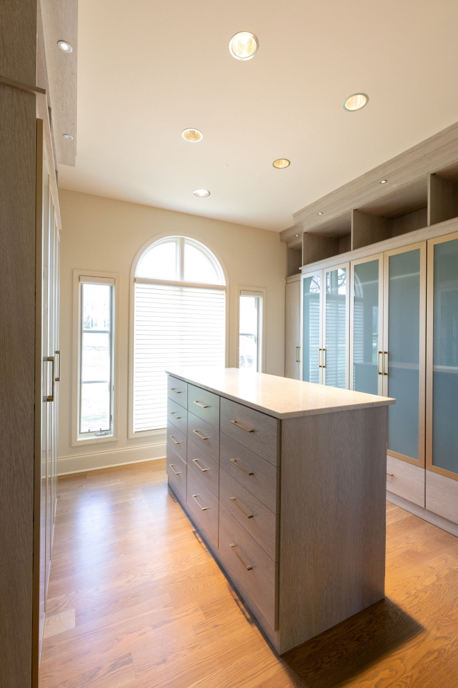 Design ideas for a large modern gender neutral walk-in wardrobe in Kansas City with glass-front cabinets, light wood cabinets and light hardwood flooring.