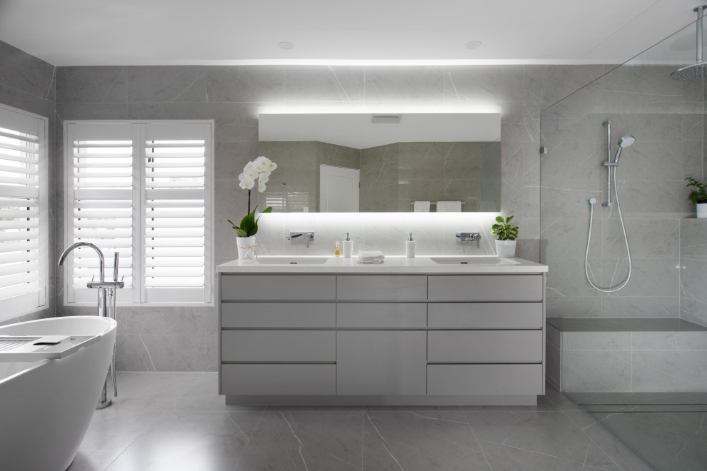 Photo of a large modern master bathroom in Brisbane with grey cabinets, a freestanding tub, an open shower, gray tile, ceramic tile, grey walls, ceramic floors, an undermount sink, engineered quartz benchtops, grey floor, an open shower, white benchtops, a shower seat, a double vanity and a built-in vanity.